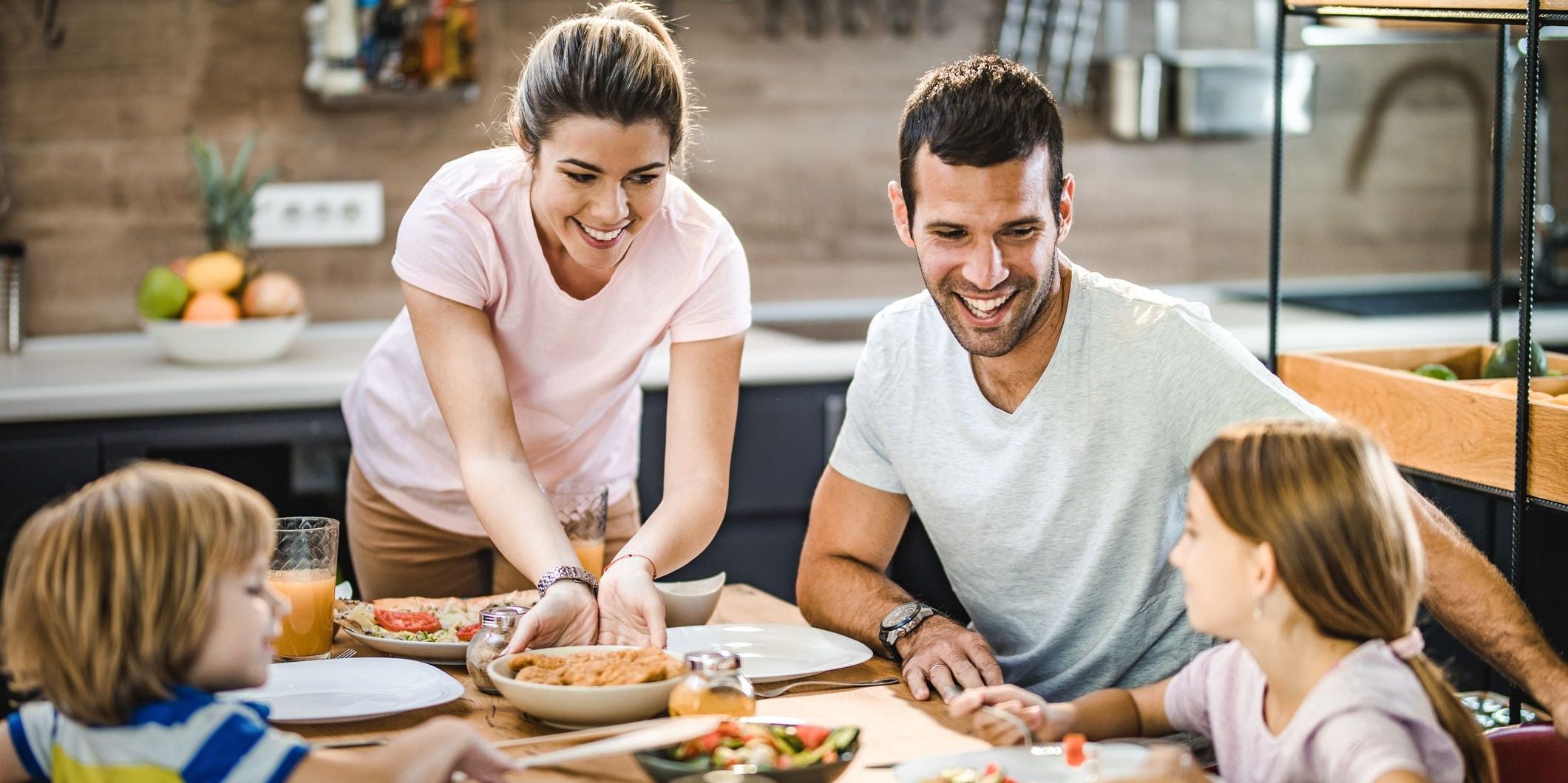 A smiling family of four enjoy a meal together at the dining table