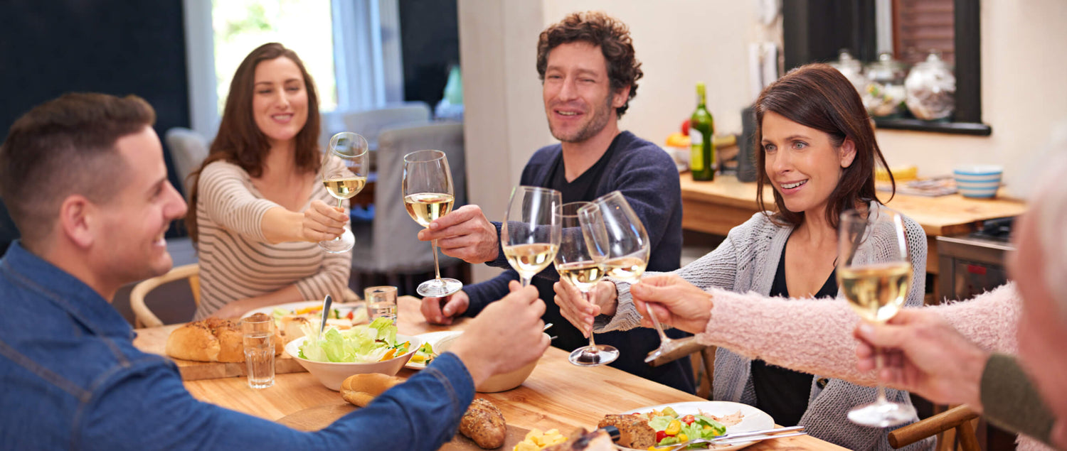 Friends gather around a dining table to eat and raise their glasses in a toast